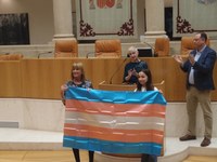 Nicole, miembro Chrysallis, hace entrega de la bandera trans a la Presidenta de la Cámara